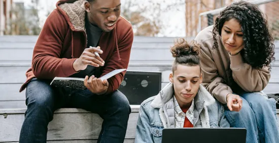 students studying on laptop with notebook on steps