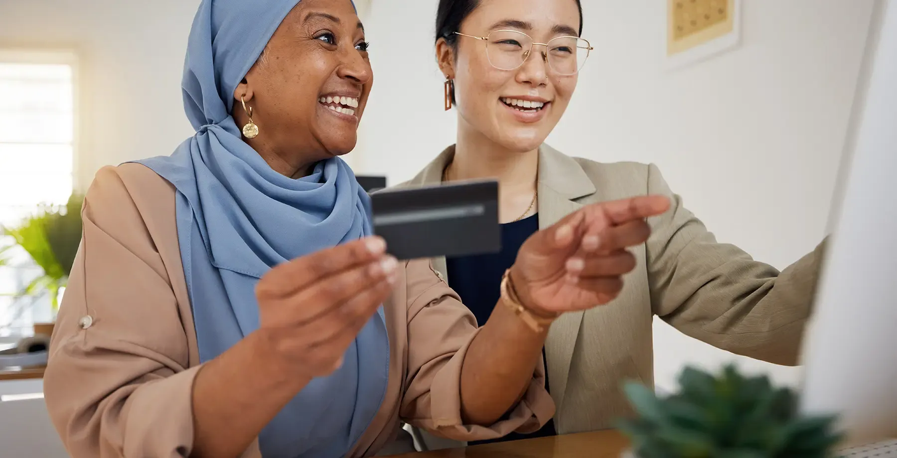 smiling women are seated at a desk in front of a computer